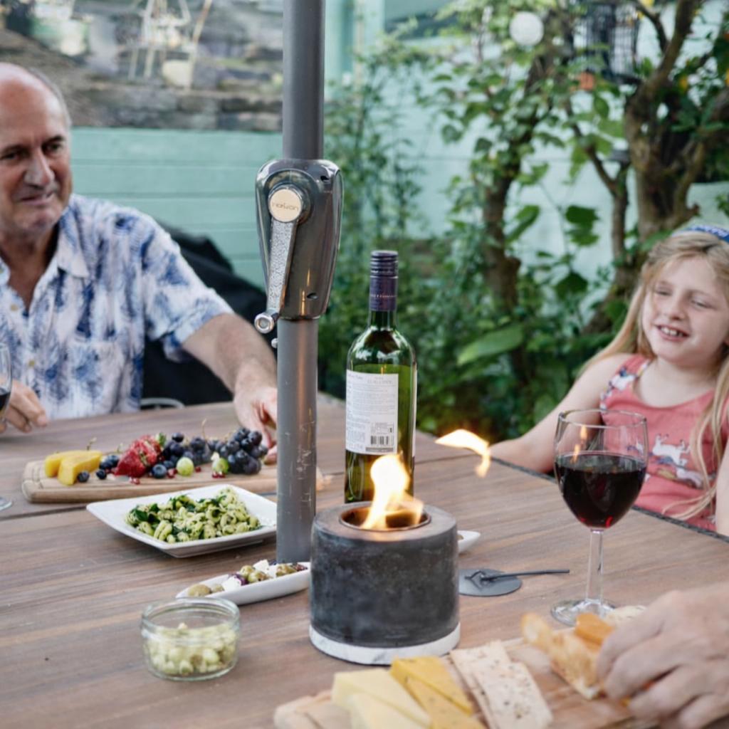 People enjoying a meal outdoors with a portable candle holder and wine bottle.